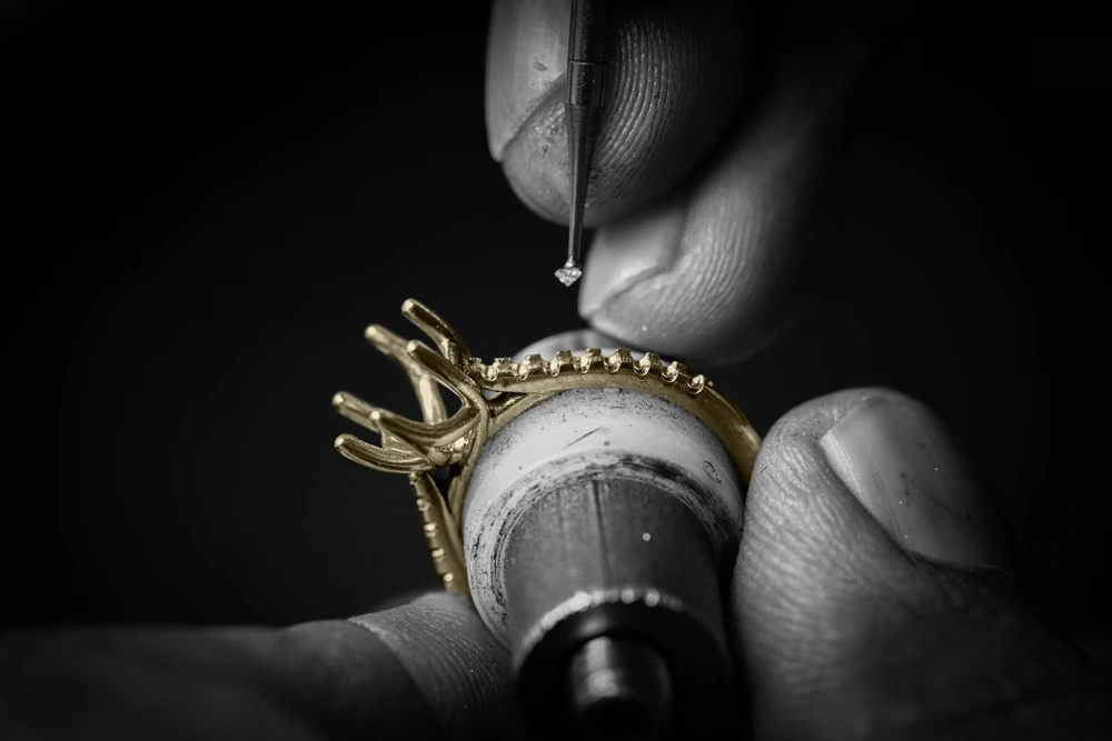 Jeweler hand-setting diamonds into a gold engagement ring setting