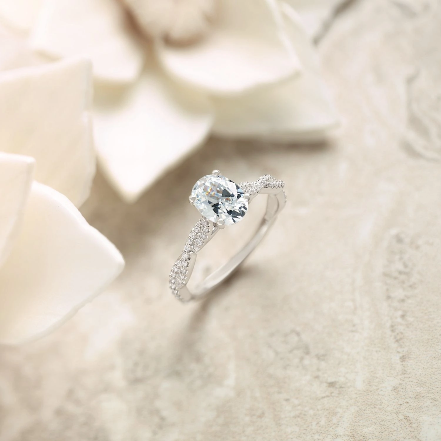 Oval diamond engagement ring with split pavé band on white marble