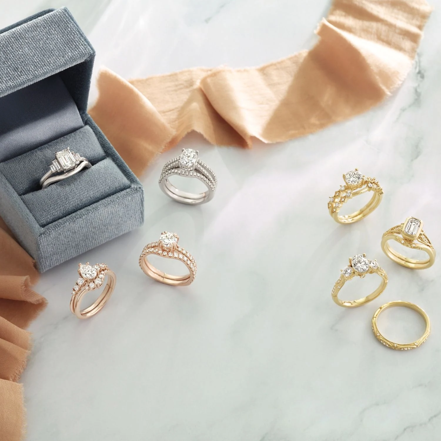Rose gold white gold and yellow gold engagement rings displayed on marble with peach ribbon
