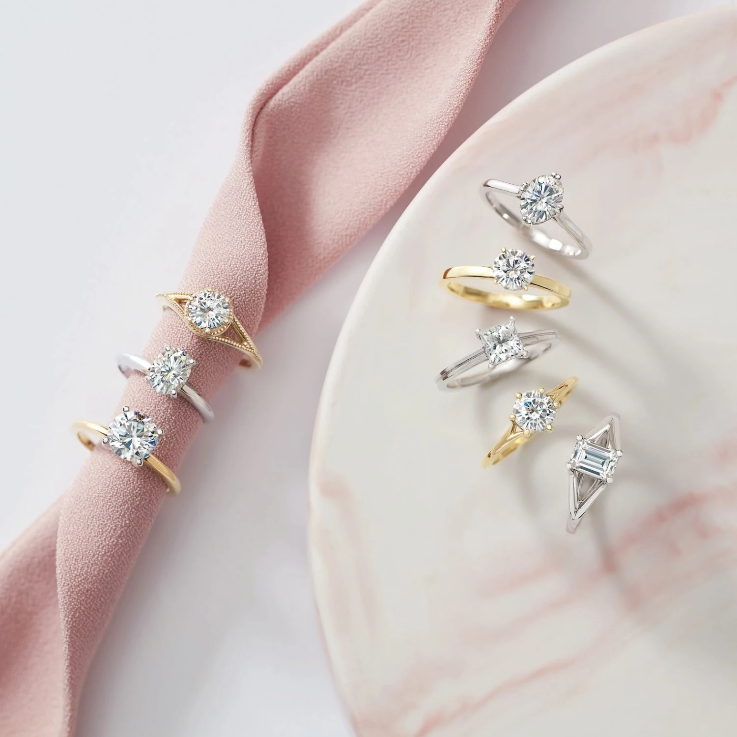 Gold and silver solitaire diamond rings arranged on pink sash and marble plate