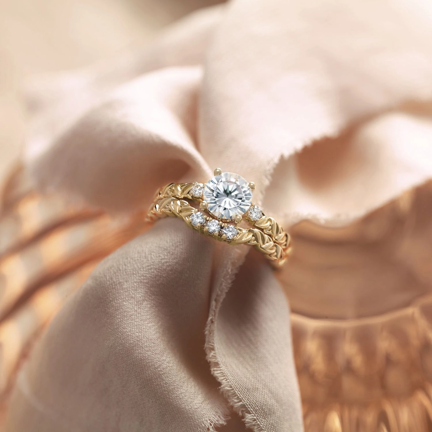 Yellow gold round diamond ring with leaf-detailed band on cream fabric
