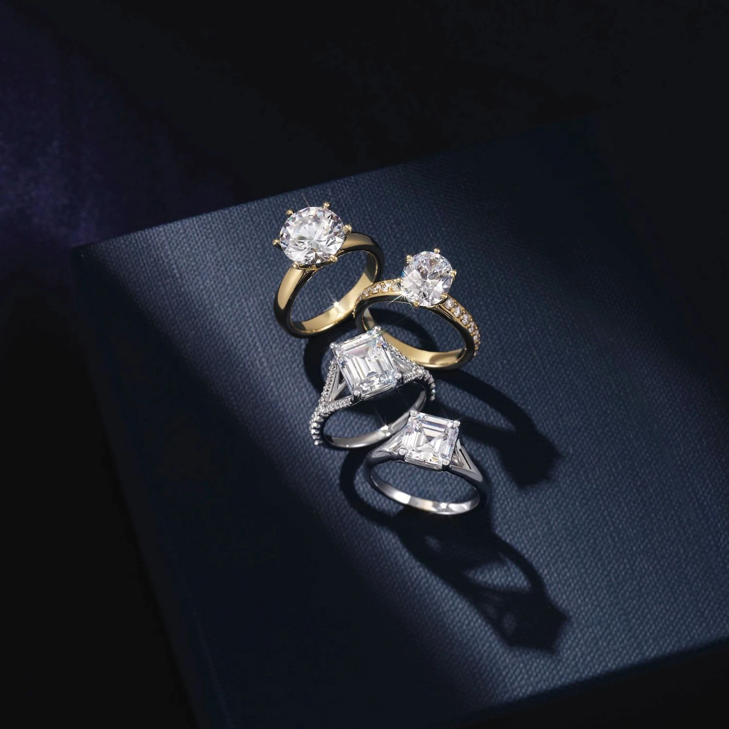 Gold and platinum emerald cut and round diamond rings on dark navy surface