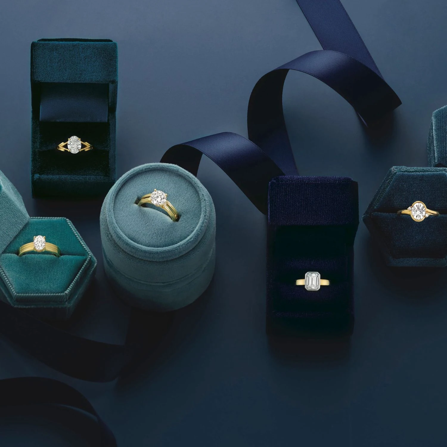 Collection of gold diamond engagement rings in velvet boxes on dark teal background