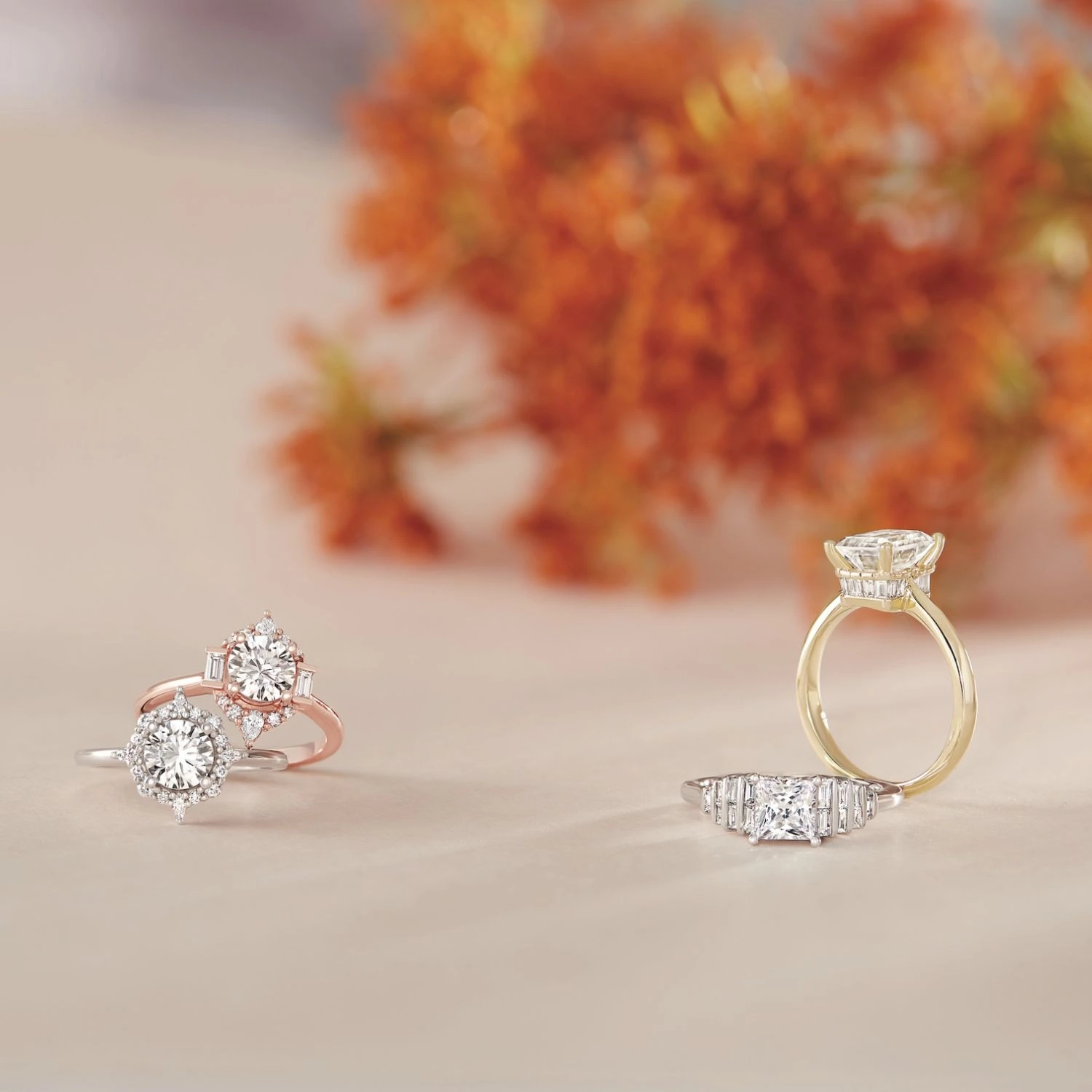 Rose gold and yellow gold diamond engagement rings with orange floral backdrop