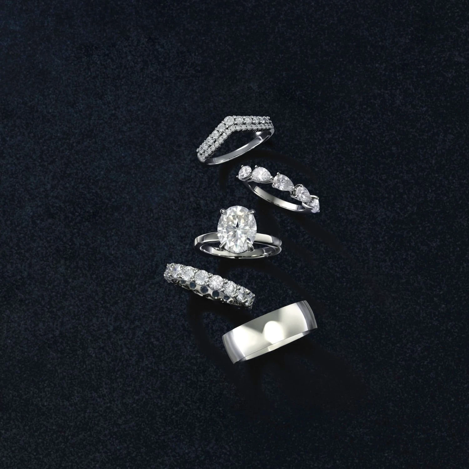 White gold diamond rings including oval solitaire and pavé band on dark velvet