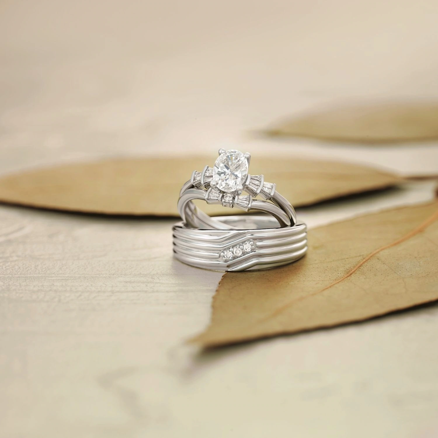 White gold oval diamond engagement ring with matching curved wedding band on dried leaves
